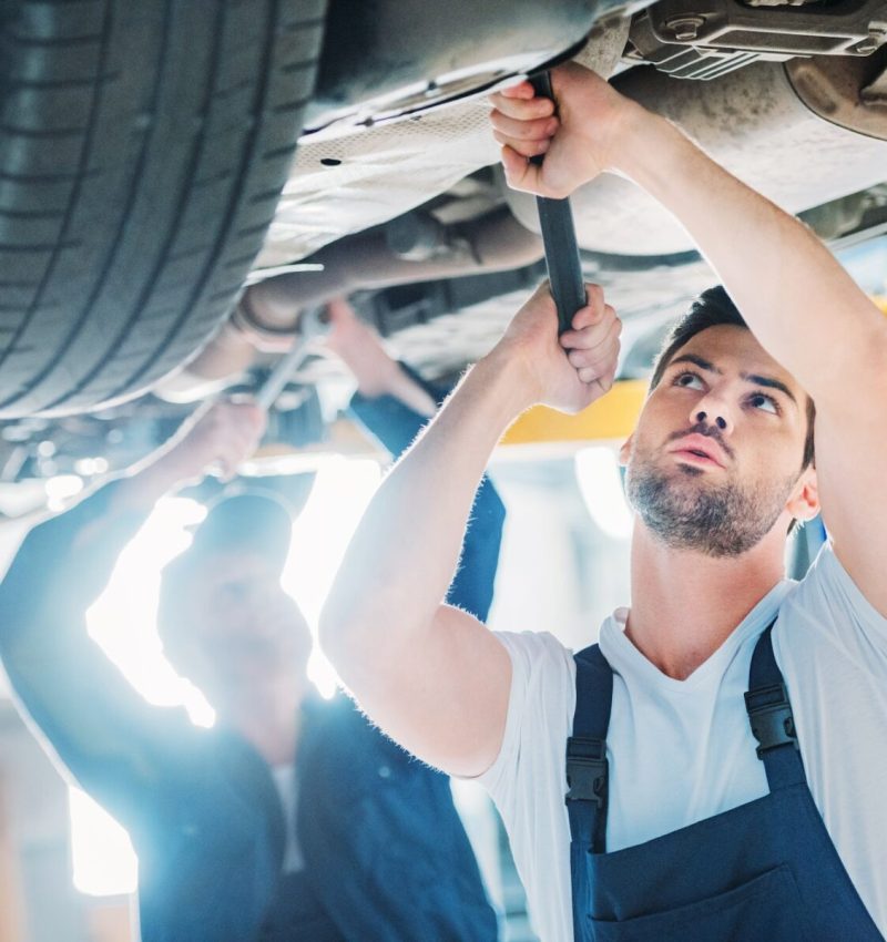Two automechanics working on a car in a repair workshop.